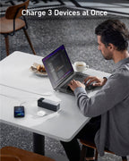 Anker 737 power bank charging a laptop, phone, and earbuds on a table.