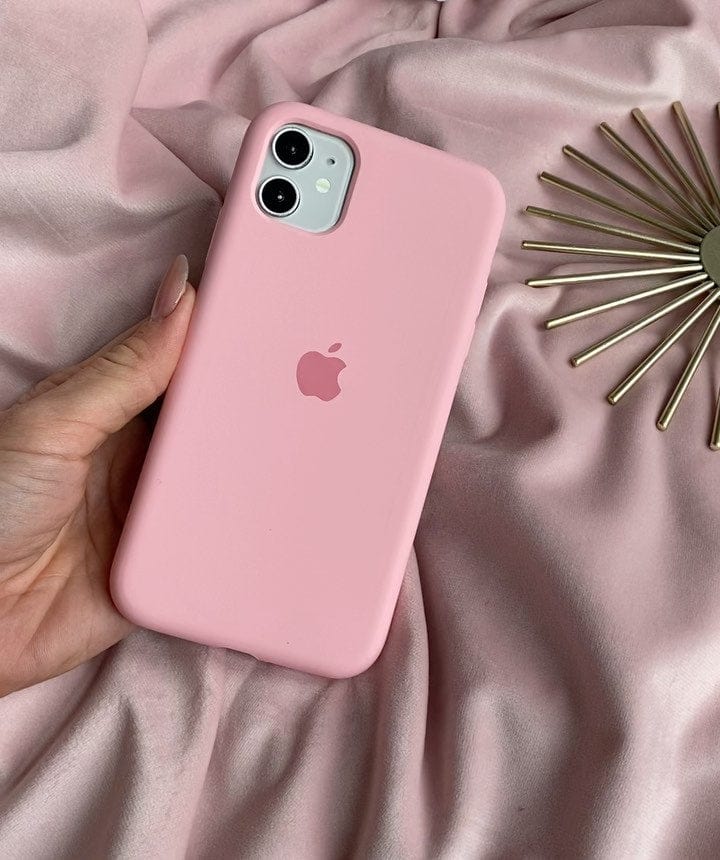 Hand holding a dual-camera iPhone in a candy pink silicone case against pink fabric.