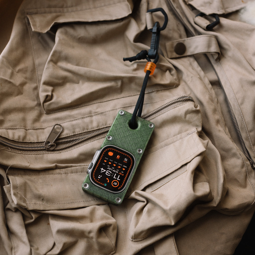 Olive green miniPhone Ultra case and Apple Watch Ultra secured to a tan vest with a cord and clip.