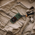 Apple Watch Ultra in an olive green miniPhone Ultra case lying diagonally on a tan vest.