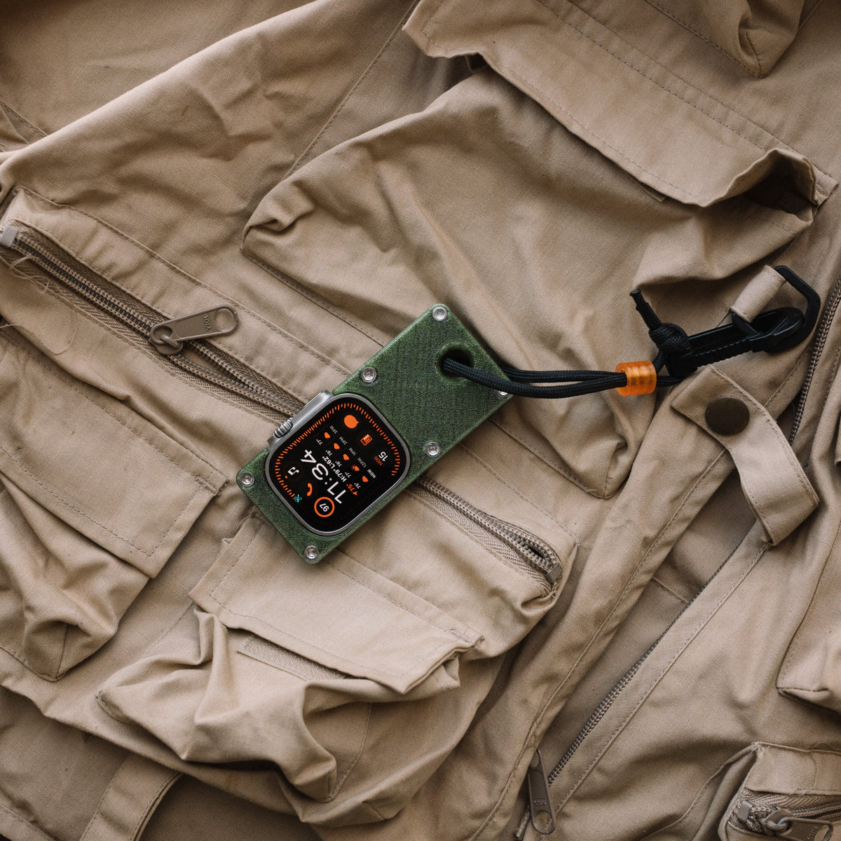 Apple Watch Ultra in an olive green miniPhone Ultra case lying diagonally on a tan vest.